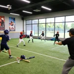 Hitclub young athletes training in a vibrant indoor batting facility, showcasing teamwork and skill development.